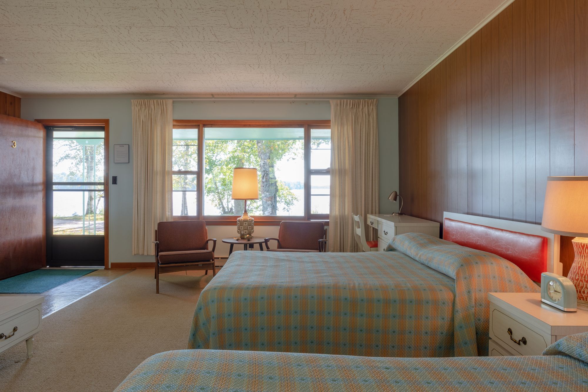 Een hotelkamer met twee bedden, een bureau, een stoel, een lamp en uitzicht op het omliggende landschap.