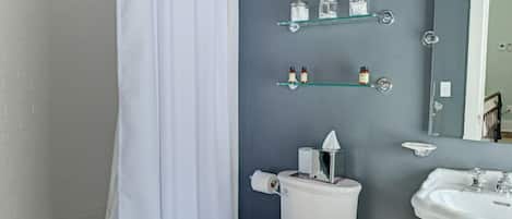Un baño con ducha, inodoro, lavabo y estantes de almacenamiento.