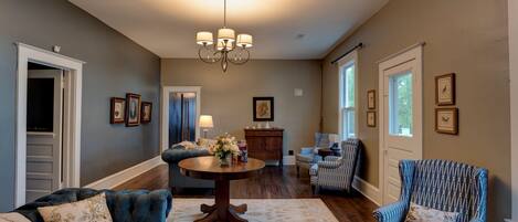 A spacious living room with a chandelier, a round table, and a blue armchair.