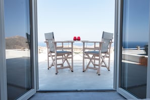 A balcony with a table and two chairs, overlooking a mountainous landscape. - Wabi Luxury Suites (Ios)