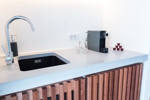 Una cocina moderna con un lavamanos de acero inoxidable, una cafetera integrada y un armario de madera.
