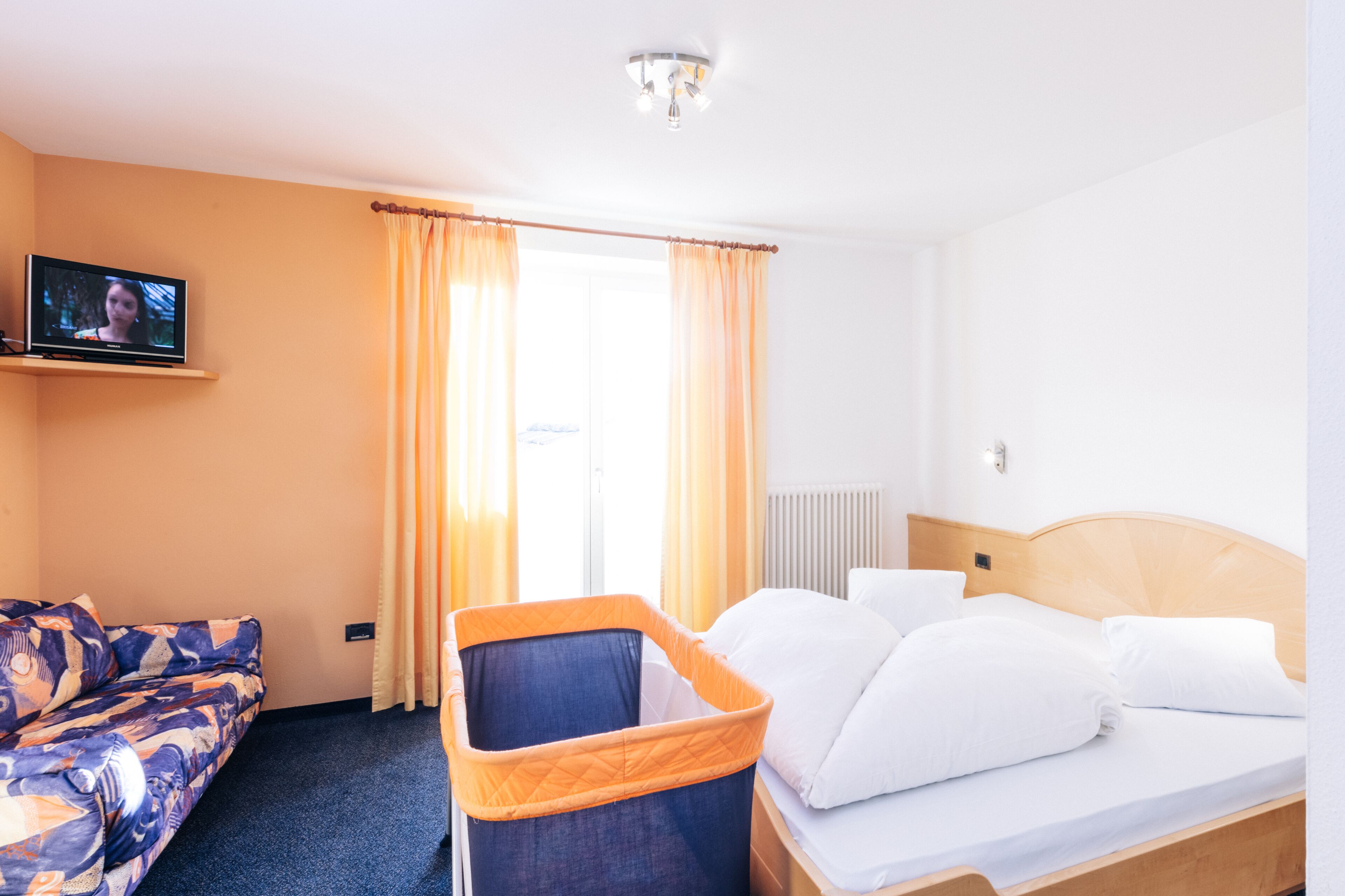 A hotel room with a bed, a sofa, a TV, and a window with curtains.