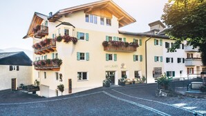 A multi-story building with balconies adorned with flowers, a cobblestone street, and a sign reading "zum Löwen". - Zum Löwen-Post Hotel (Trodena)