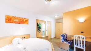 A hotel room with a bed, a desk, and a chair. There is a door leading to a bathroom and a hallway. - Zum Löwen-Post Hotel (Trodena)