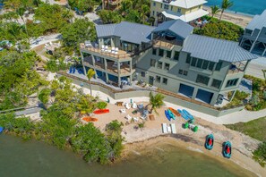 Ein mehrstöckiges Anwesen direkt am Strand mit Pool, Liegestühlen und Bootsanleger.