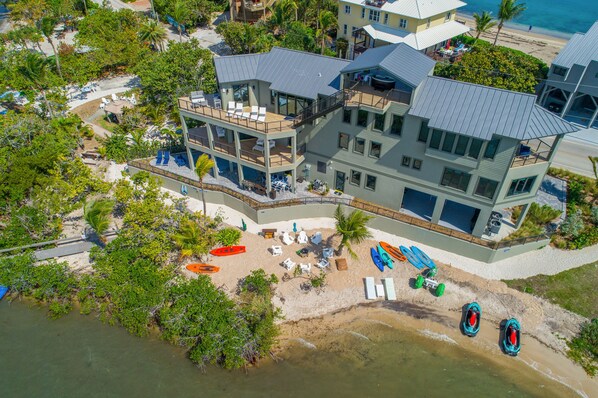 A multi-story beachfront property with a pool, beach chairs, and a boat dock.