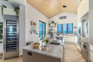 A modern kitchen with a central island, stainless steel appliances, and a view of the sea through large windows.