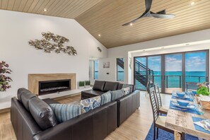 A modern living room with a fireplace, a large sofa, and a view of the sea through large windows.
