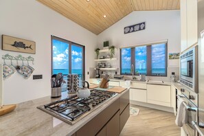 A modern kitchen with a large island, stainless steel appliances, and a view of the sea through large windows.
