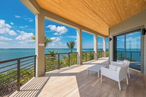 A covered outdoor area with a view of the sea, featuring a seating area with white furniture and a wooden ceiling.