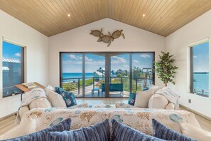 A bedroom with a large window overlooking a balcony with a view of the sea.