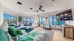A spacious bedroom with a large bed, a seating area with a view of the sea, and a TV displaying various streaming services. - Nirvana Shores: Ocean-2-River FL Beach House w/heated pool,dock,elevator,hot tub (Stuart)