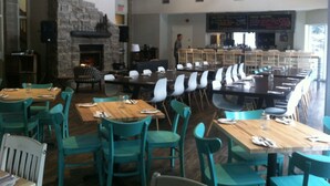 A restaurant with multiple dining tables and chairs, a stone fireplace, and hanging pendant lights.