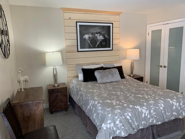 A bedroom with a bed, two bedside tables, a chair, a wooden headboard, a framed picture, and a wardrobe.