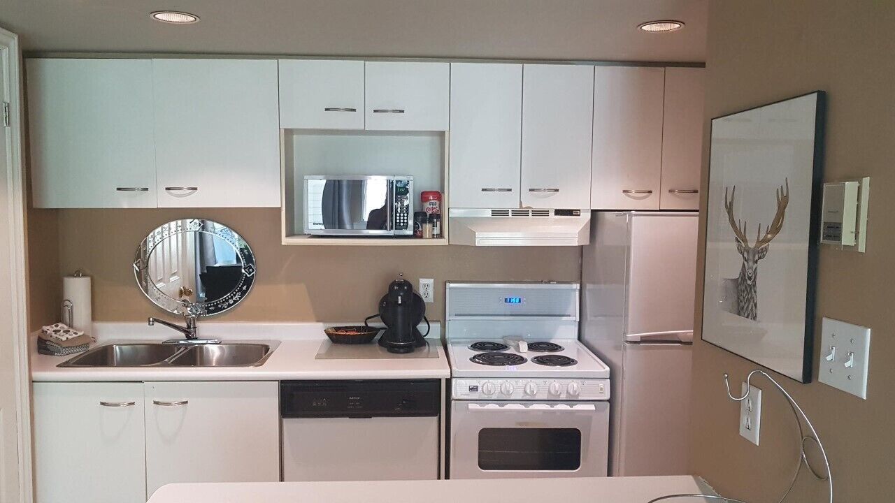 A compact kitchen with white cabinets, a microwave, a stove, and a sink.