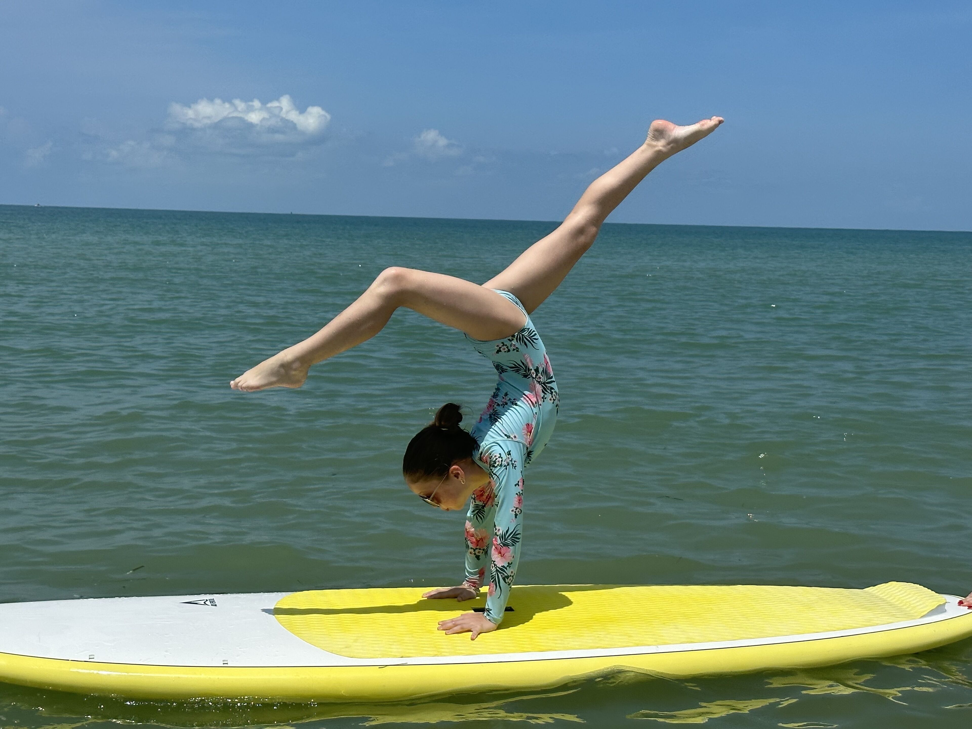 A person performing a handstand on a yellow surfboard in the ocean.