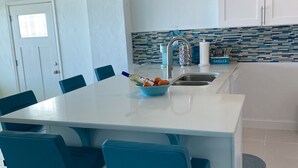 Una cocina moderna con una isla central, sillas azules y luces colgantes.