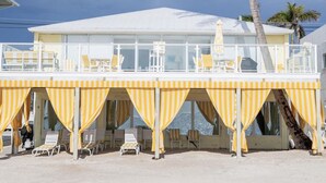 Un edificio frente a la playa con techo blanco, toldos a rayas amarillas y sillas de descanso.