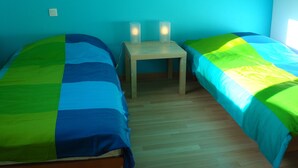 Een kamer met twee eenpersoonsbedden, een klein tafeltje en een stopcontact.