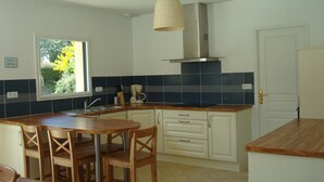 Een keuken met een houten tafel en stoelen, een raam met uitzicht op bomen, en een deur.