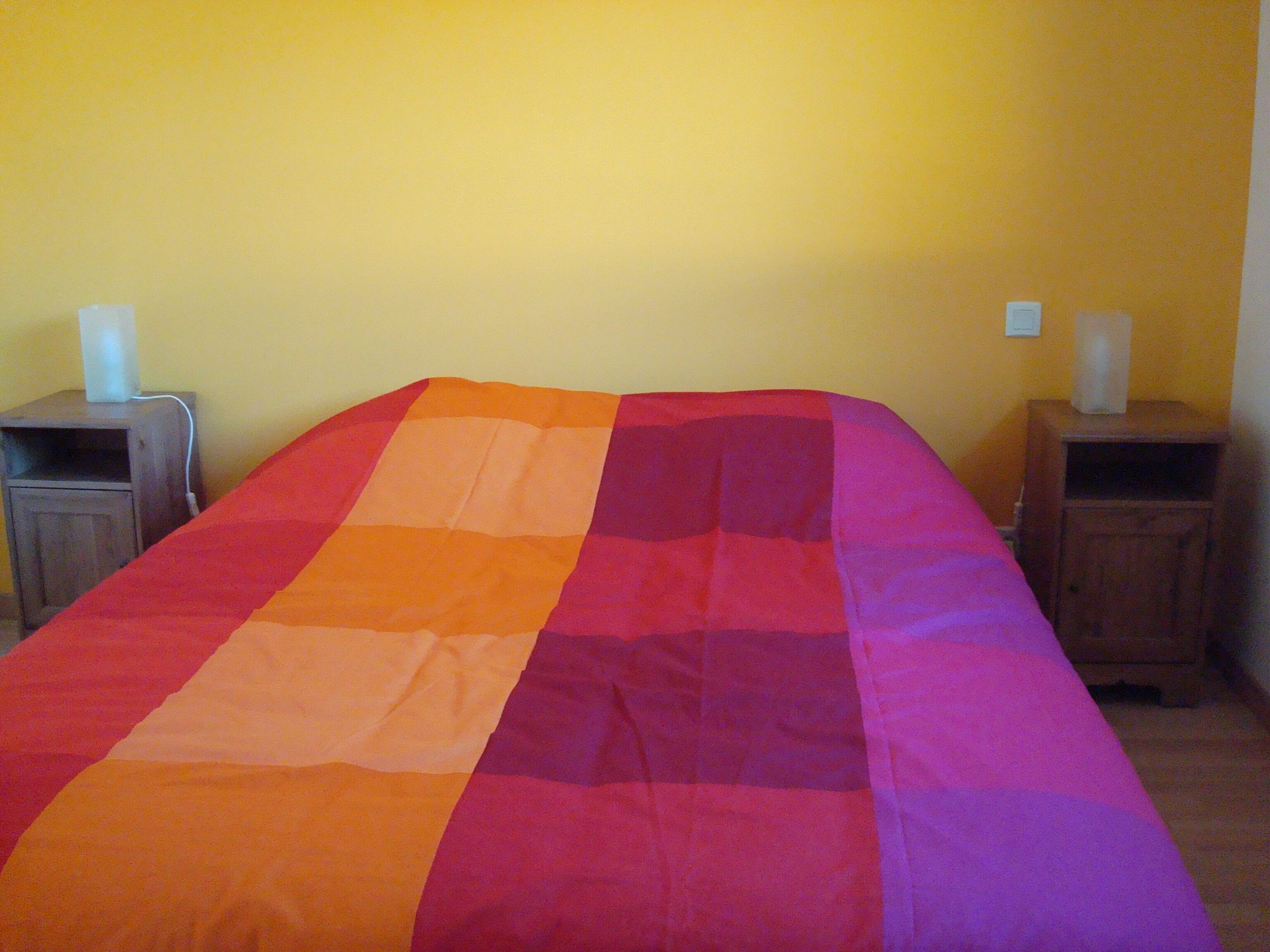 Un llit amb un llençol multicolòr, dues tauletes de nit i una paret groga.