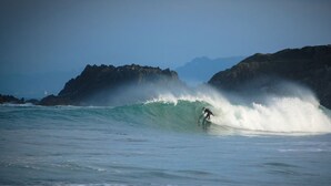 Een surfer die een grote golf rijdt, met rotsachtige kliffen op de achtergrond.