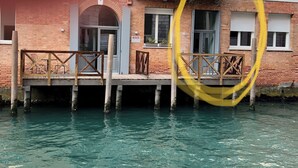 A brick building with a wooden dock extending into a body of water. - Canal view with terrace Luxury LOFT (Venezia)
