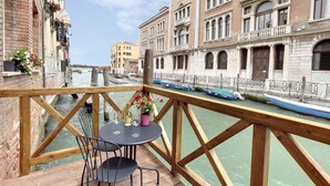 A balcony with a wooden railing overlooking a canal with boats, featuring a table with chairs and a potted plant. - Canal view with terrace Luxury LOFT (Venezia)