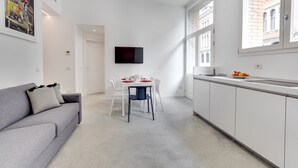 A modern kitchen with white cabinets, a dining table with chairs, and a grey sofa with a pillow. - Canal view with terrace Luxury LOFT (Venezia)