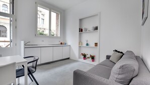 Une cuisine moderne avec des meubles blancs, une table à manger avec des chaises et un canapé gris agrémenté d’un coussin.