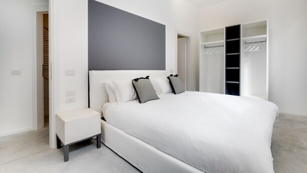 A modern bedroom with a large bed, a bedside table, a walk-in closet, and a gray accent wall. - Canal view with terrace Luxury LOFT (Venezia)