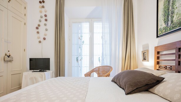 A bedroom with a bed, a television on a side table, a wicker chair, and a painting on the wall. - Lovely apartment in the historic district of Seville (+ WiFi & AC) (Sevilla)