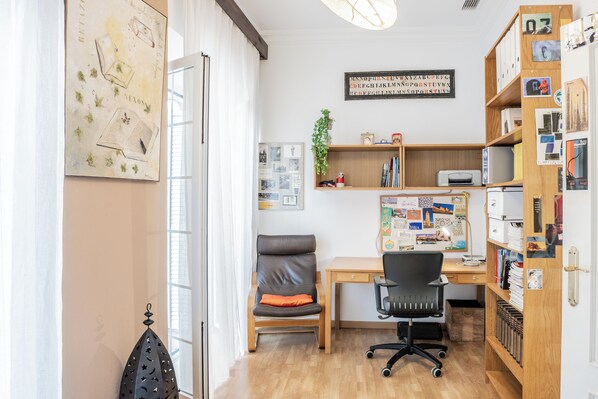A well-lit office space with a desk, office chair, bookshelf, and a wall with various items and decorations.