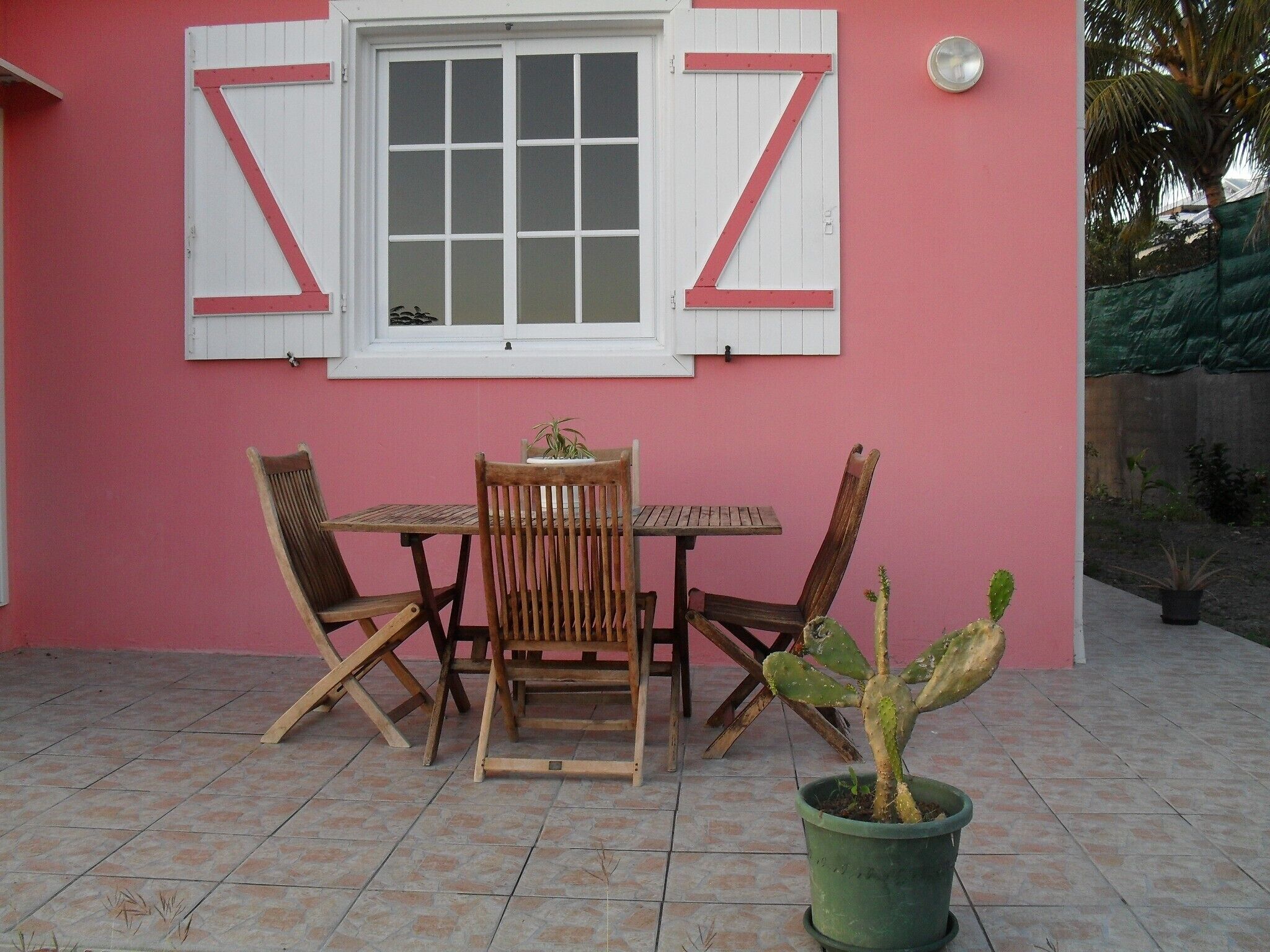 A patio with a wooden table and chairs, a potted cactus, and a window with shutters.