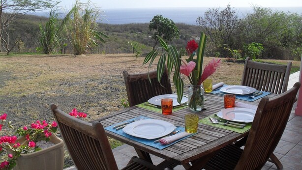 A wooden table set outdoors with chairs, plates, cutlery, and a vase with flowers. - A Deshaies F5 sea view equipped for families / groups nearby beaches   (DESHAIES)