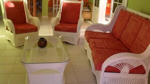 A living room with white wicker furniture, including two armchairs and a sofa, all with red cushions. A glass coffee table with a decorative item on it is in the center. - A Deshaies F5 sea view equipped for families / groups nearby beaches   (DESHAIES)