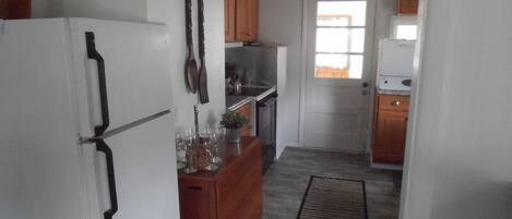 Ett kompakt kök med ett kylskåp, träskåp, ett matbord med stolar, en liten köksö med en växt och en takfläkt.