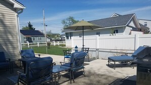 An outdoor patio with blue chairs and a table, a grill, and a covered umbrella.