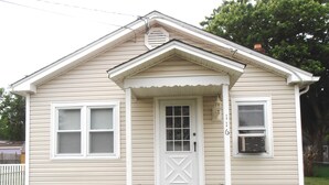 A single-story house with a front porch, a white door, and two windows on the side.