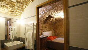 A bathroom with a stone wall, a wooden dresser, a bed with an orange pillow, and a white sink.