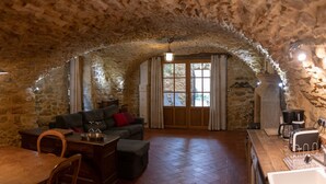 A stone-walled room with a wooden dining table, a sofa, and a kitchen area with a toaster.
