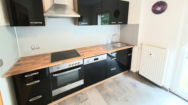 A modern kitchen with black cabinets, a stainless steel oven, a built-in dishwasher, and a wooden countertop.