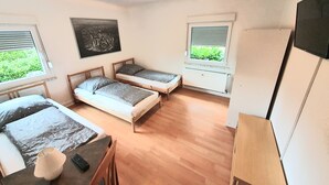 A small, well-lit room with two single beds, a table with a lamp, and a TV on a stand.