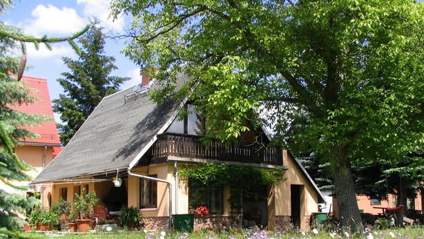 Una casa tradicional con techo inclinado, un balcón y un jardín lleno de flores.