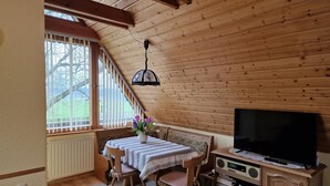 Una habitación acogedora con techo de madera, una mesa con sillas, un televisor y una ventana con persianas.