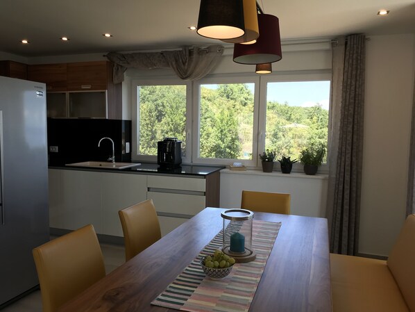 A modern kitchen with a dining area, large windows, and a view of greenery. - Brand new, with infinity pool, right by the pool (Brsec)