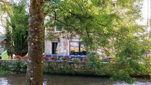 Un restaurant a la riba del riu amb terrassa, parets de pedra i vegetació.