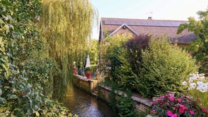 Un canal estret amb vegetació exuberant a banda i banda, una paret de pedra i un edifici amb teulades al fons.