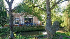 Un edifici rústic amb façana de pedra, un mur de maó i un petit canal d'aigua.