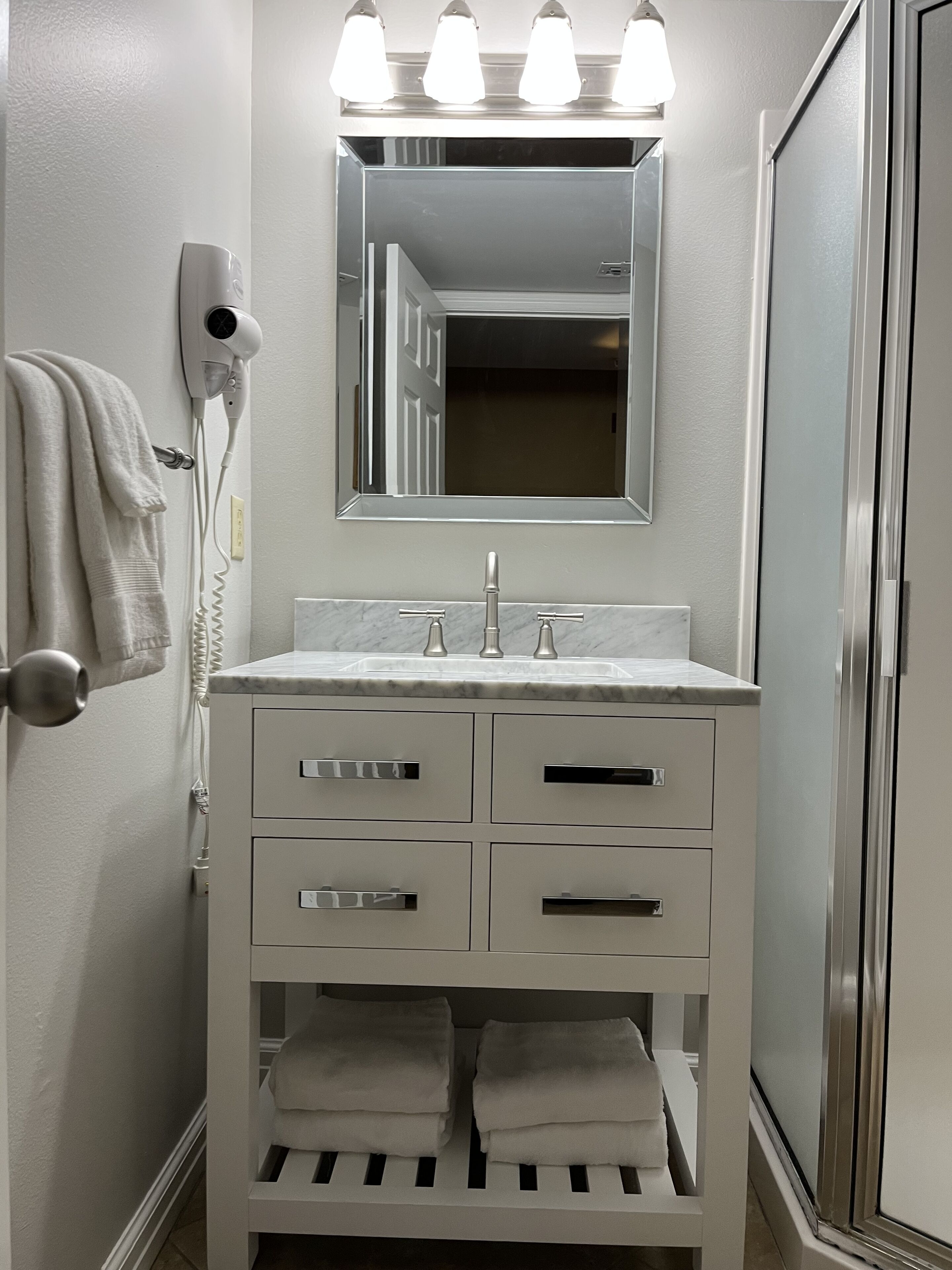 Une salle de bain moderne avec un meuble-lavabo blanc, un miroir, un sèche-cheveux et un porte-serviettes.